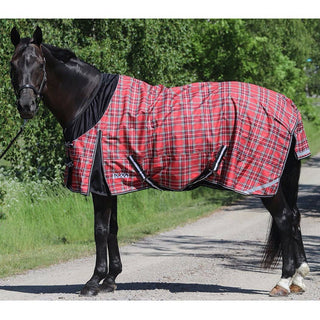En svart häst som står på en grusväg. Hästen har på sig nova  freedomtäcke i svart röd ruta och svart softshell mot halsen och i bogvecket. 